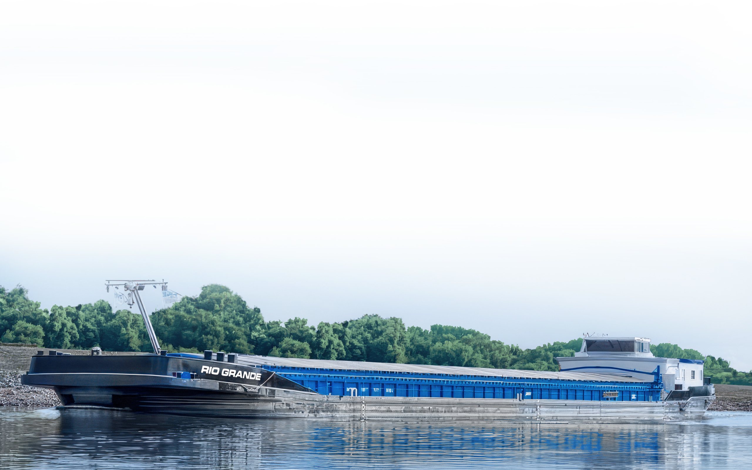 A long, black and blue barge named LEANORA navigating a wide river, surrounded by dense, green forested banks under a clear sky